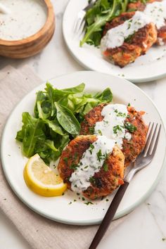 two white plates topped with chicken patties next to a green salad and lemon wedges