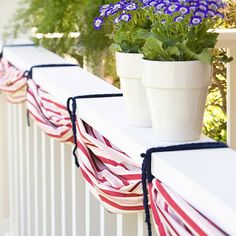 some flowers are sitting in a pot on a balcony railing with red, white and blue striped curtains