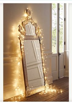 a large mirror sitting on top of a wooden floor next to a window covered in fairy lights