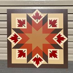 an image of a quilt with red and brown leaves on the center, in front of a building