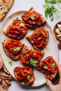 a plate with slices of bread topped with sliced tomatoes and basil next to other ingredients