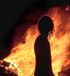 a person standing in front of a fire with their head turned to the side and arms outstretched