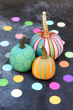 three painted pumpkins sitting on top of a table with colorful polka dot circles around them