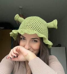 a woman wearing a green crocheted hat with two horns on her head, smiling