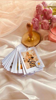 a stack of magazines sitting on top of a bed next to a vase with flowers