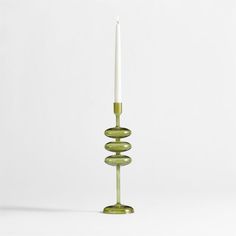 a green candle holder sitting on top of a white table next to a tall glass candle