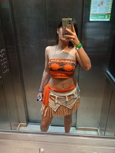 a woman taking a selfie in front of a mirror wearing an orange top and fringe skirt