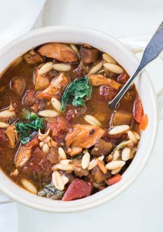 a white bowl filled with meat and bean soup on top of a table next to a spoon