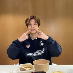 a young man sitting at a table with food in front of him and pointing to the side