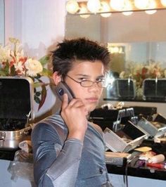 a man standing in front of a counter talking on a cell phone while wearing glasses