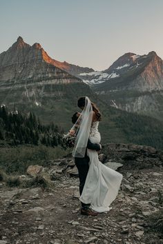 a bride and groom standing on top of a mountain with mountains in the back ground