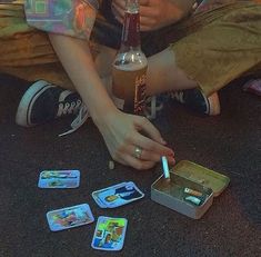 a person sitting on the ground holding a bottle and playing with cards