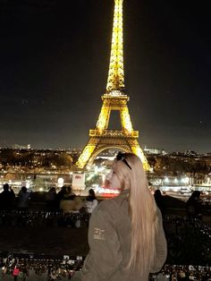 a woman with long hair standing in front of the eiffel tower at night