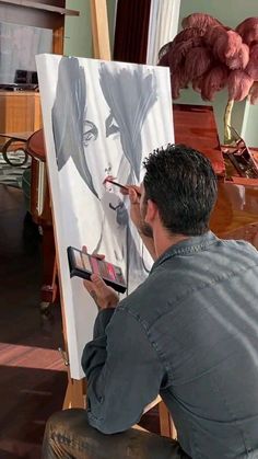 a man sitting in front of an easel painting