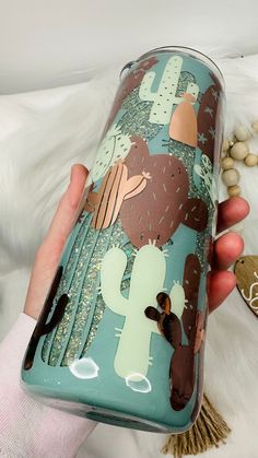 a person holding a cup with cactus designs on it and white fur in the background