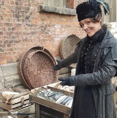 a woman is standing in front of an old basket and smiling at the camera,