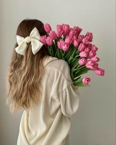 a woman holding a bouquet of pink tulips with a bow on her head