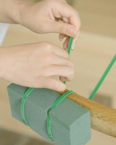 a person holding a piece of green tape on top of a wooden stick with a block of paper tied to it