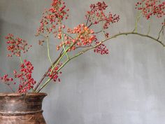 a vase filled with red flowers on top of a wooden table next to a wall