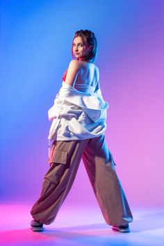 a woman in white top and brown pants posing for the camera with her arms behind her back