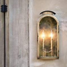 an old fashioned wall light with two candles on it's side, against a stucco wall