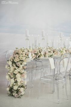 the table is set up with clear chairs and white flowers on each chair, along with candles