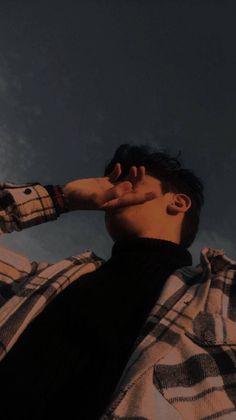 a man with his hand on his head looking up into the sky while wearing a plaid shirt