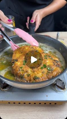 a person cooking food in a pan on top of a stove with pink tongs