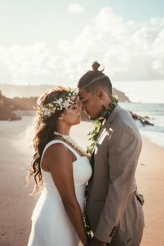 a man and woman standing on top of a beach next to the ocean with flowers in their hair