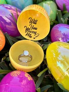 an assortment of colorful easter eggs with wedding rings in the middle and will you marry me? written on them