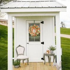 a small white shed with two chairs and a wreath on it's front door