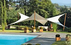 an outdoor swimming pool surrounded by trees and bushes with two large white tents in the background