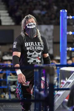 a man with long hair wearing a black mask and wrestling gear in front of a crowd