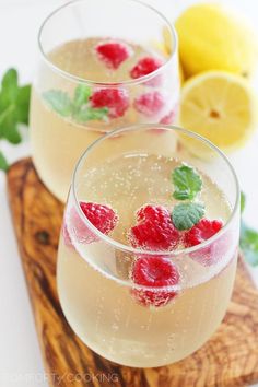 two glasses filled with ice and raspberries on top of a wooden cutting board