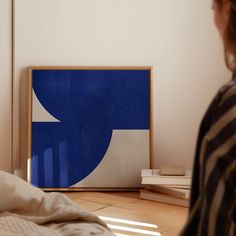 a woman standing in front of a blue and white painting on the wall next to a bed