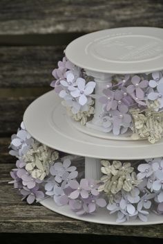 three tiered white cake with purple flowers on each layer, sitting on top of a wooden table