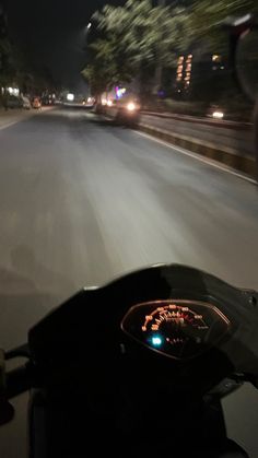 a motorcycle driving down the road at night time with its lights on and it's dashboard lit up