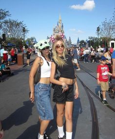 two women standing next to each other in front of a castle with people walking around