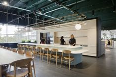 two women are standing at the counter in an open office space with chairs and tables