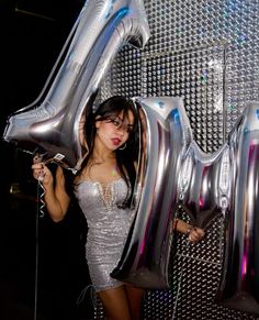 a woman in a silver dress is holding some balloons that spell out the number twenty