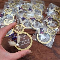 a person holding up some wedding rings and brooches in plastic bags on a wooden table