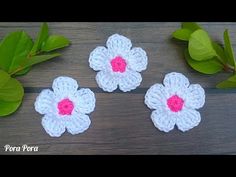 three crocheted flowers sitting on top of a wooden table next to green leaves