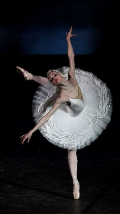 the ballerina is dressed in white and has her arms stretched out as she stands on one leg