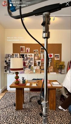 a desk with a lamp on top of it in front of a wall covered with pictures