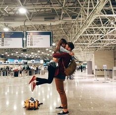 two people are hugging in an airport with luggage on the ground and signs above them