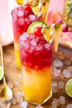 two glasses filled with drinks sitting on top of a wooden table next to sliced pineapples