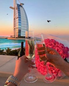 two people are toasting with wine glasses in front of the burj al arab hotel