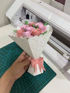 someone is holding a bouquet of flowers in front of a machine that cuts out paper