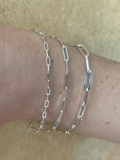 three different types of chain bracelets on someone's arm, one is silver and the other is white