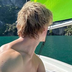 a young man sitting on top of a boat in the ocean next to a green sailboat